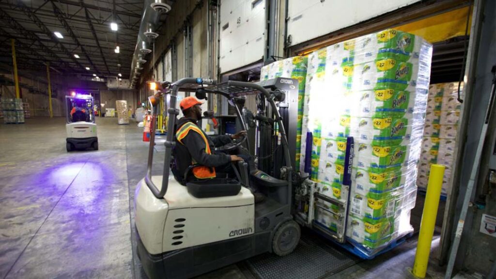 Stapelfahrer in einer Lagerhalle befördert Paletten von Küchenpapier.