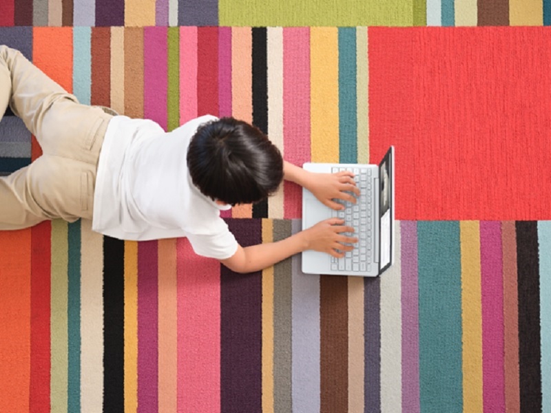 Ein Kind im Grundschulalter liegt zu Hause auf einem Teppich und arbeitet mit einem Surface.