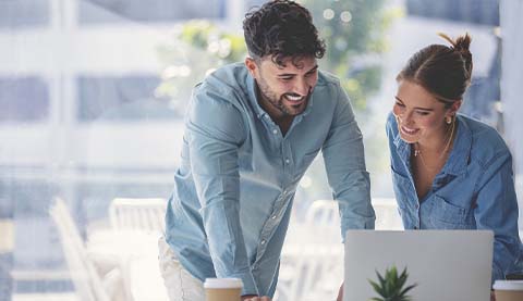 Zwei Personen lachend vor einem Laptop.