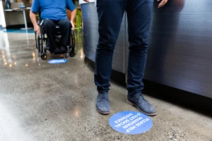 Two employees in line in a cafe obeying floor stickers to stay 6 feet apart for social distancing.