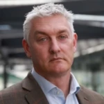 Mark Deighton, a man wearing a suit and tie smiling at the camera