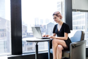 A woman using a laptop computer sitting in the office by a window