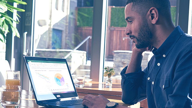 A person is sitting at desk, in front of window, working on a Surface device.
