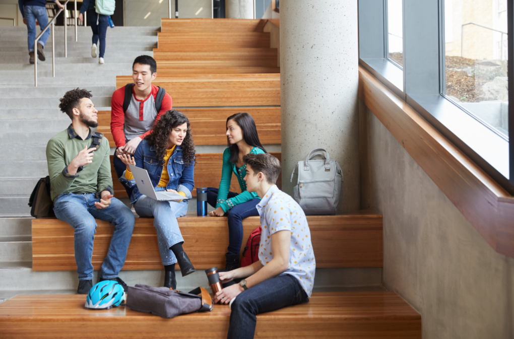 A group of male and female students seated together in an indoor common area on a university campus..