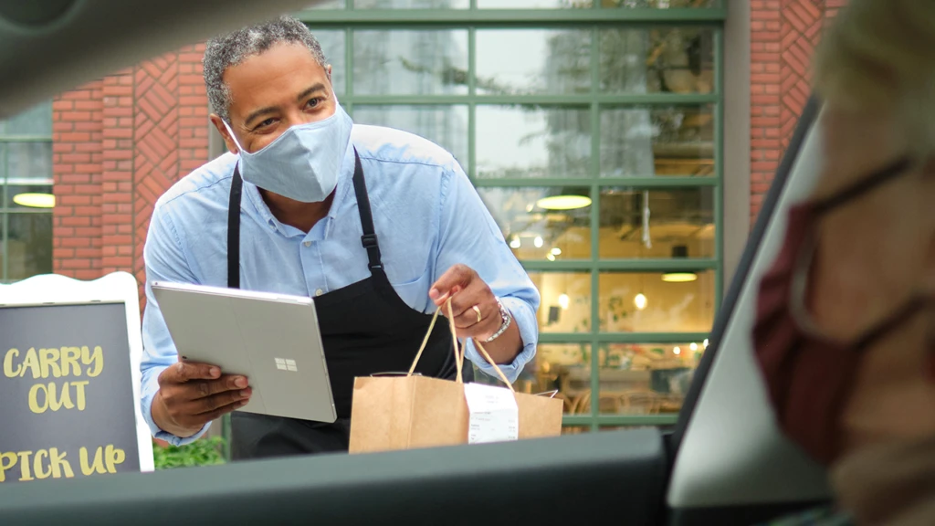 man with a mask delivering food to driver in the car