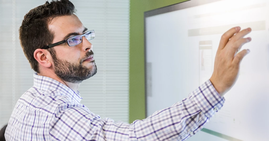 Worker standing in a modern office and using a large touchscreen monitor.