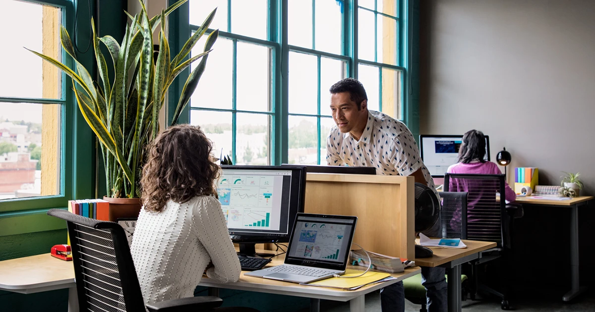 Two employees talk by their desks