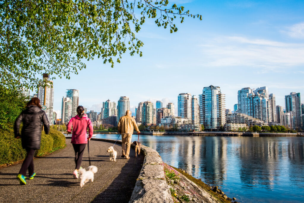 VANCOUVER, BRITISH COLUMBIA, CANADA. People walking dogs on a waterside trail with downtown skyline in the distance.