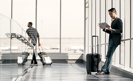 A man waits in an airport holding an electronic device.