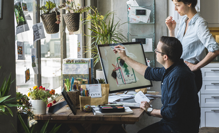 A man and woman work on a project over a desktop computer.