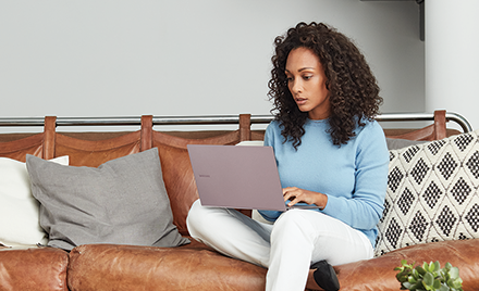 A woman sitting on a couch using her PC laptop.