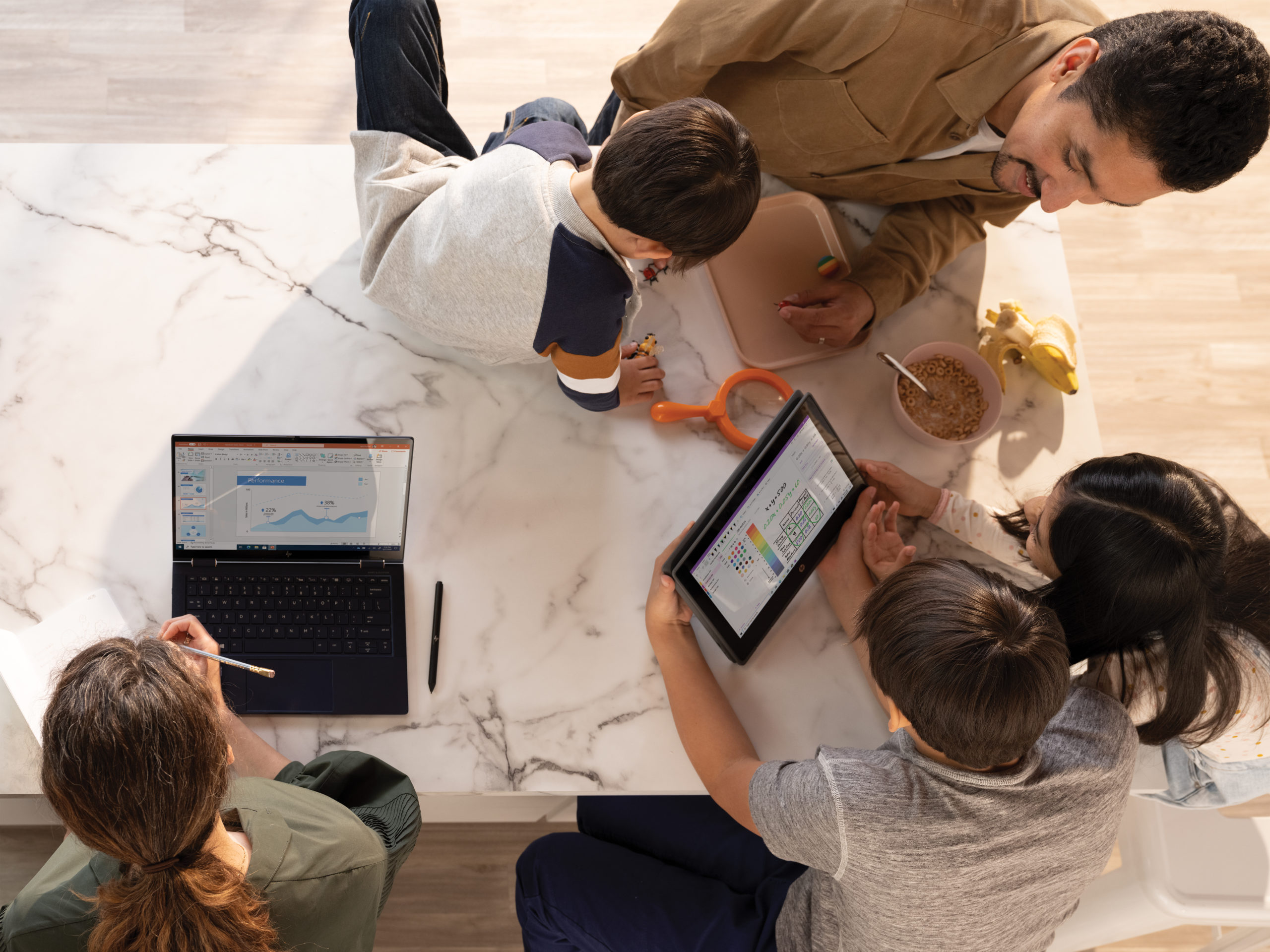 A family working and learning remotely around their kitchen table. The mother has a PowerPoint file open on an HP Elite Dragonfly. The father and two older children are looking at OneNote Math Assistant on an HP Probook x360. Remote Learning and Remote Working collections