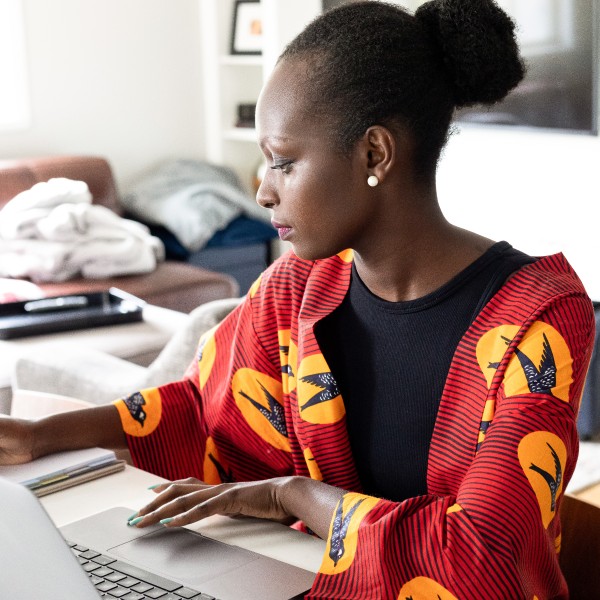 A woman working from home, sitting at a desk with a laptop, writing on a notepad.