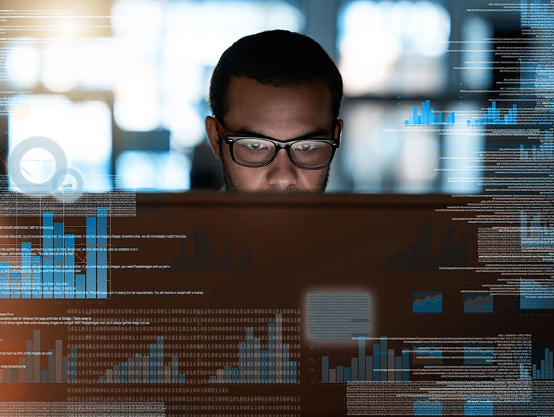 Security worker wearing glasses and looking at a computer monitor, surrounded by an overlay of code and charts