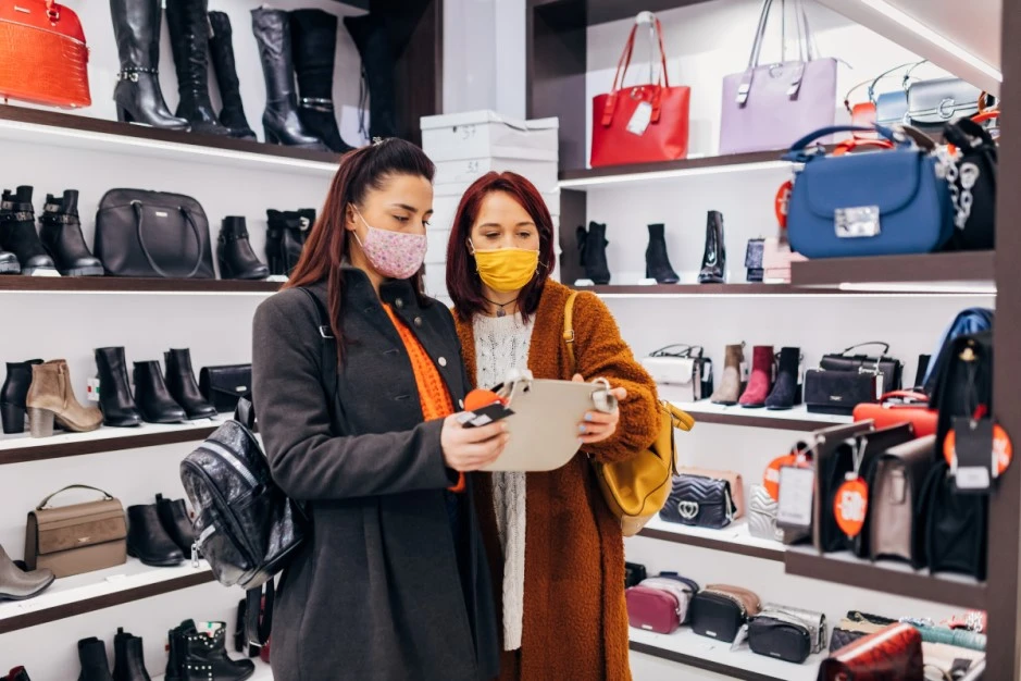 Two people in retail store looking at a handbag with masks on