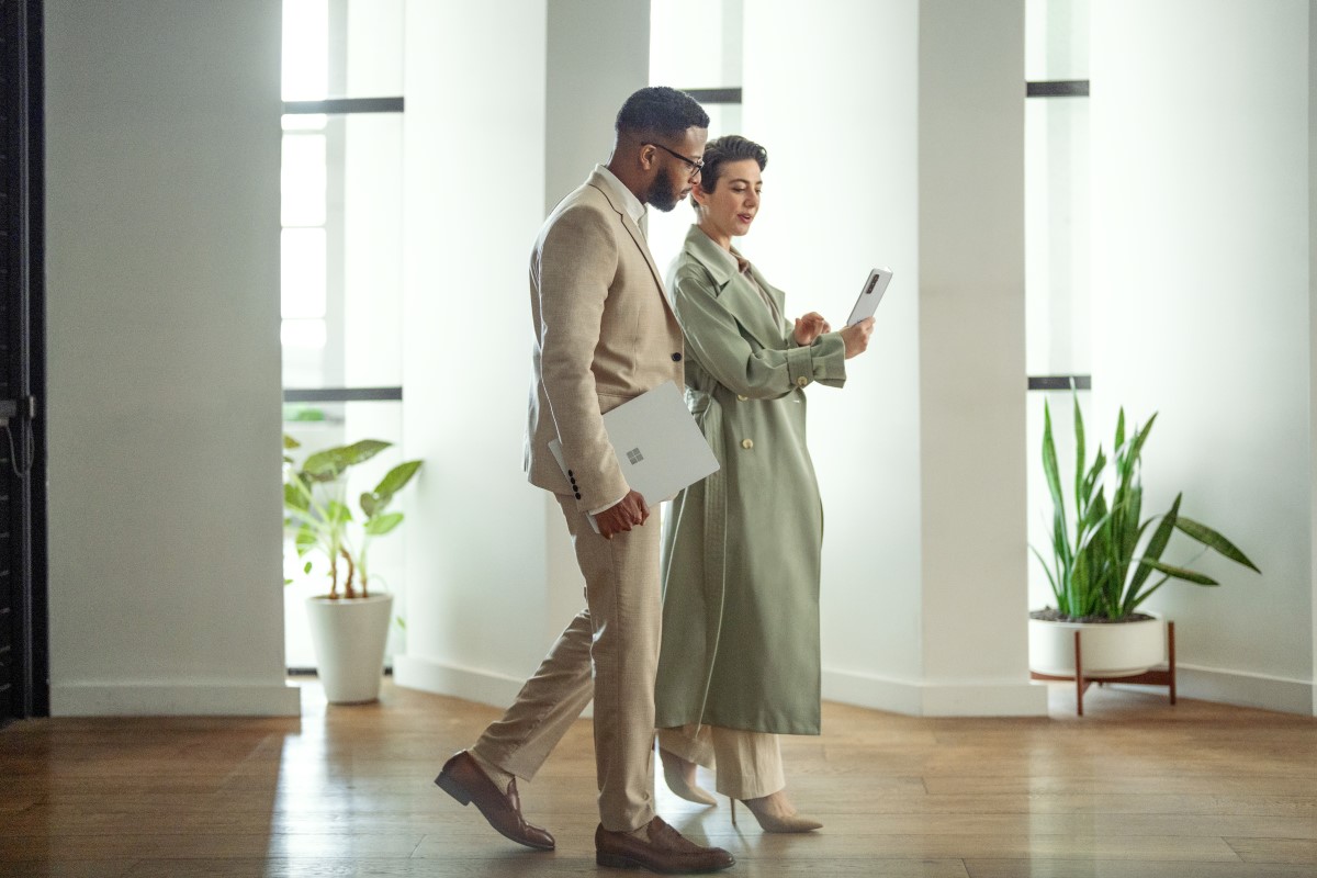 A man walking in an office holding a Surface Laptop 5 in Platinum. No screen is showing.