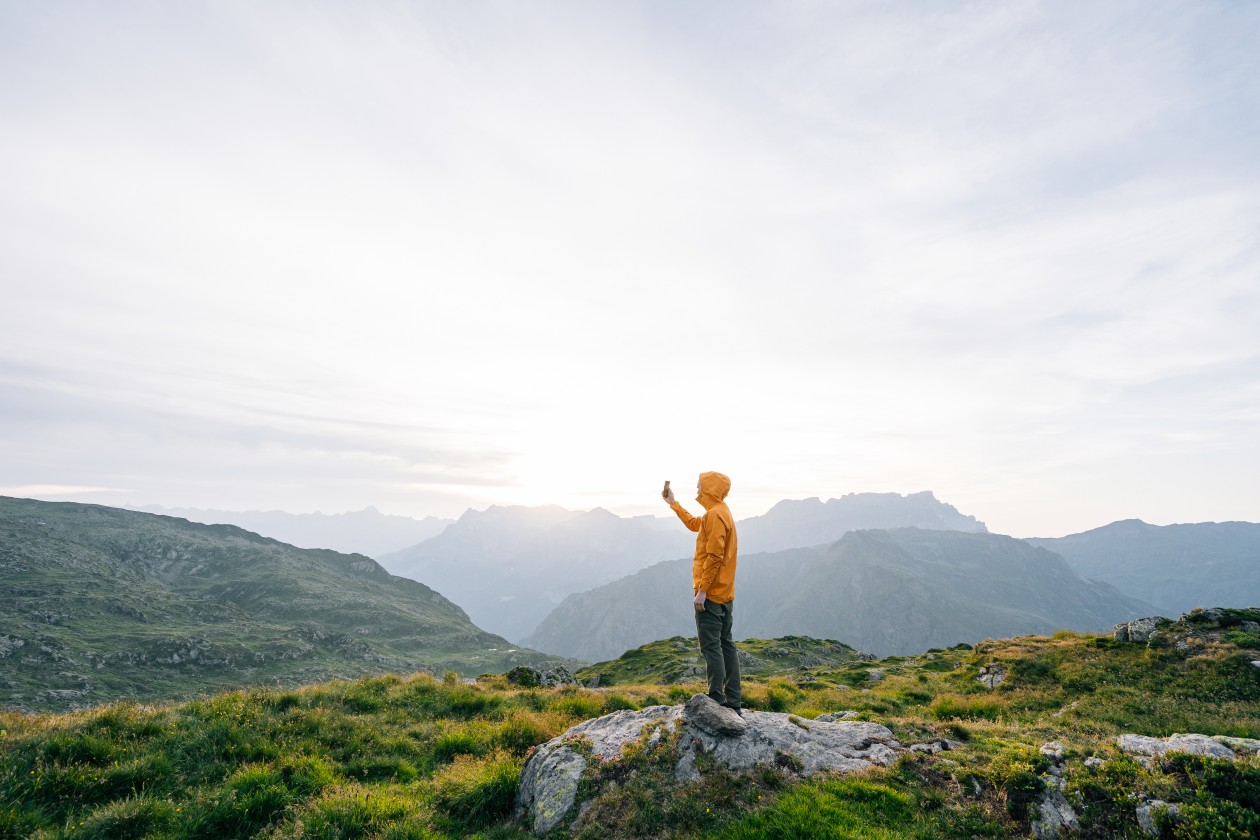 Young man takes photo with cell phone at sunrise on an alpine meadow.