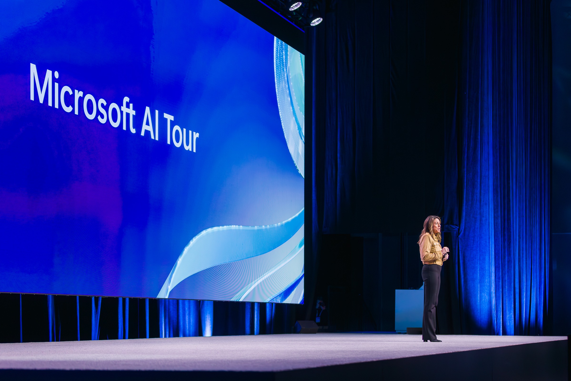 Tracy Galloway, Microsoft executive, speaking onstage at Microsoft AI Tour with a blue &ldquo;Microsoft AI Tour&rdquo; backdrop