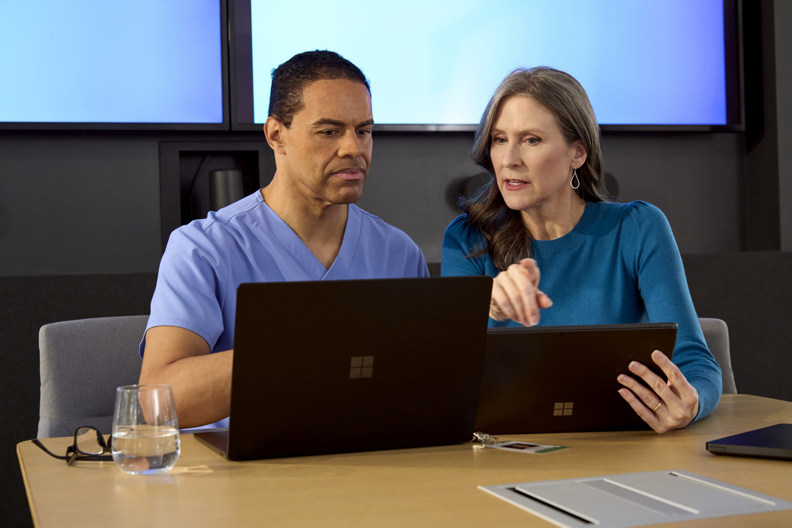 Male clinician and female hospital administrator looking at a computer and tablet in a conference room.