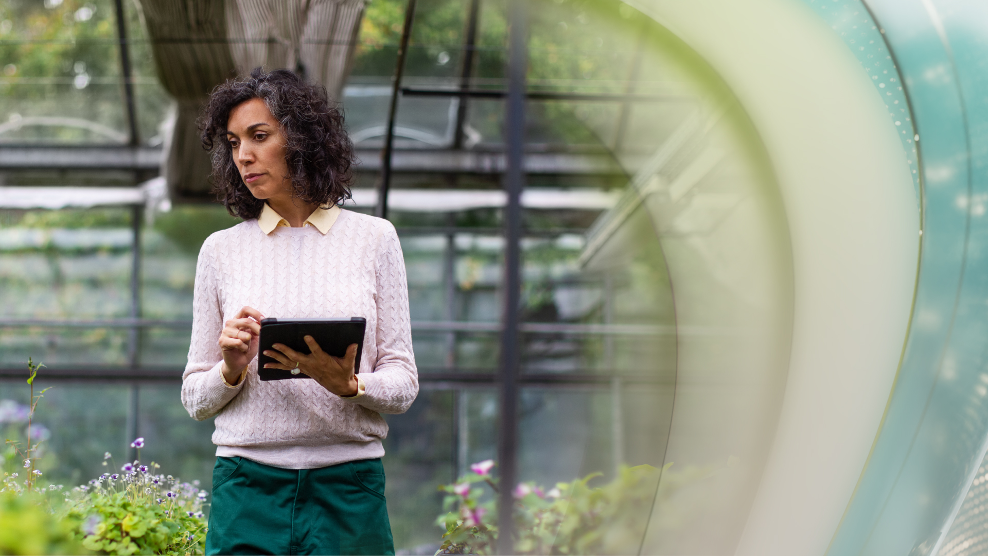 Business owner walks through her greenhouse with data on her tablet.