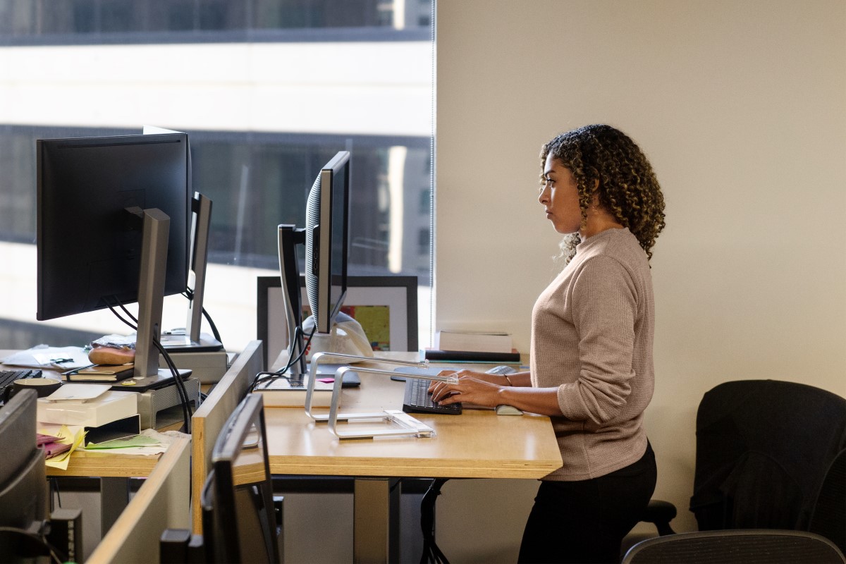 Real people, real offices. Black female developer doing focused work at a standing desk in enterprise workspace. Focused work. Women who code, women developers, women engineers, code, develop, Black developer, engineer, Visual Studio, Azure.