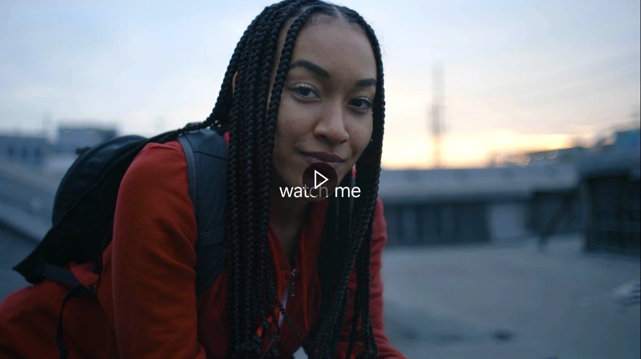 A frame from a video picturing a woman sitting down outdoors, wearing a backpack