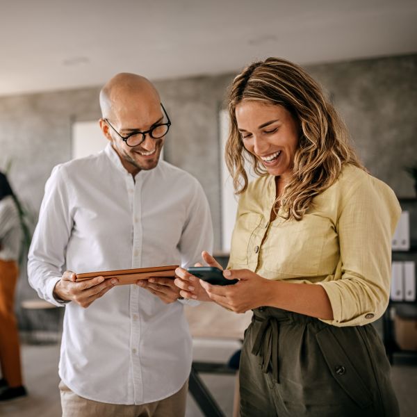 Two coworkers standing and looking at devices together.