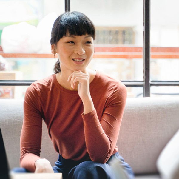 Confident young female entrepreneur sits on a couch smiling as she discusses ideas with a colleague.
