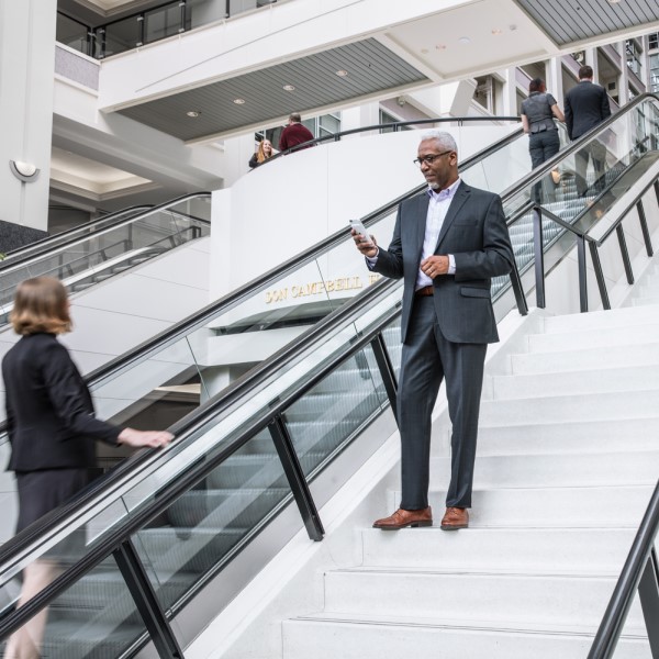 A man standing on stairs in an office building, looking at his phone.