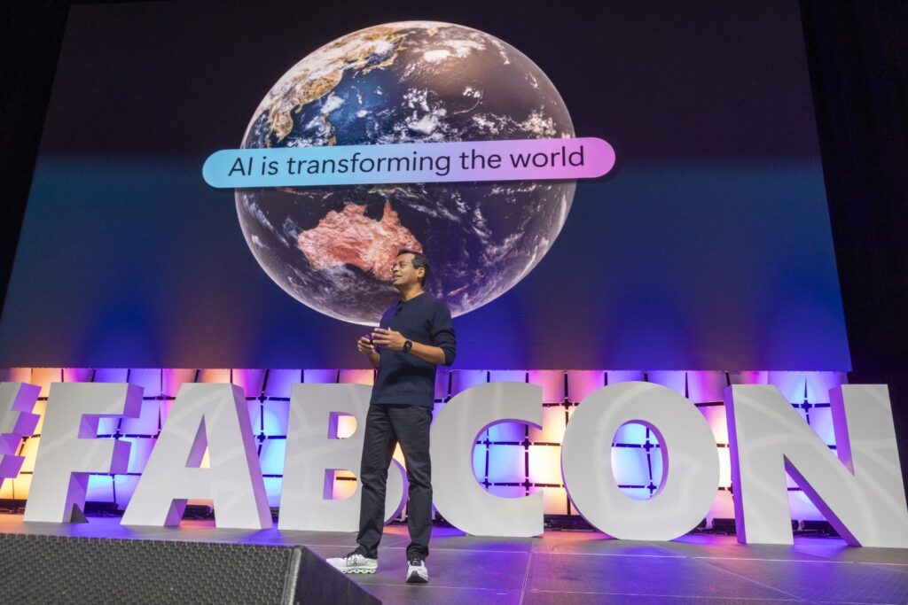 A man standing on stage with a large sign and a planet in the background