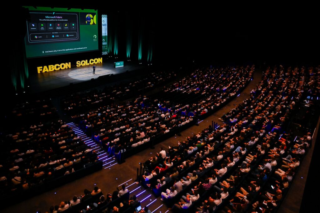 A crowd of people watching the FabCon and SQLCon stage during a presentation.