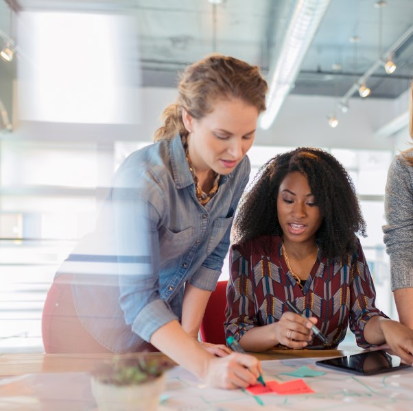 Businesswomen look at a digital tablet and discuss a project in their modern office