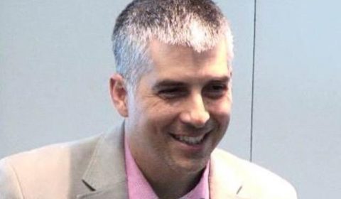 a man wearing a suit and tie smiling at the camera