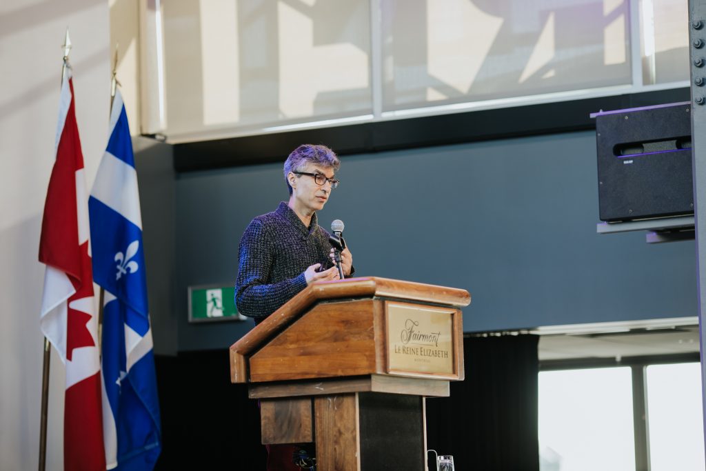 Yoshua Bengio standing in front of a television