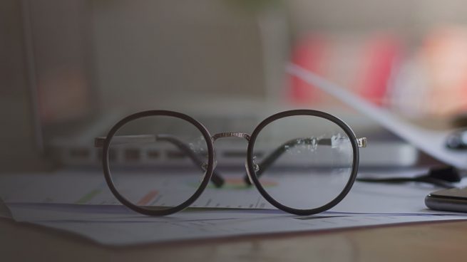 selective focus front eyeglasses on table with blur office supplies, vintage light tone.
