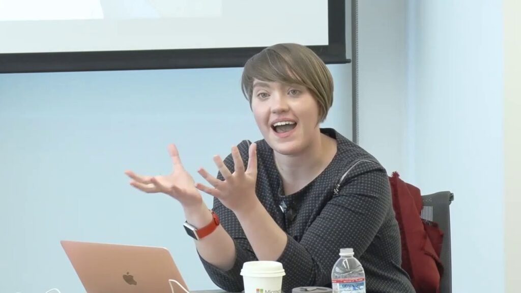 a woman sitting at a table with a laptop and smiling at the camera