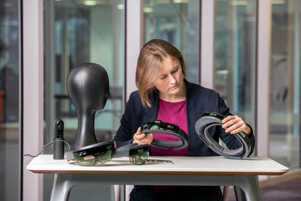 Cecily Morrison sitting at a table holding two HoloLens