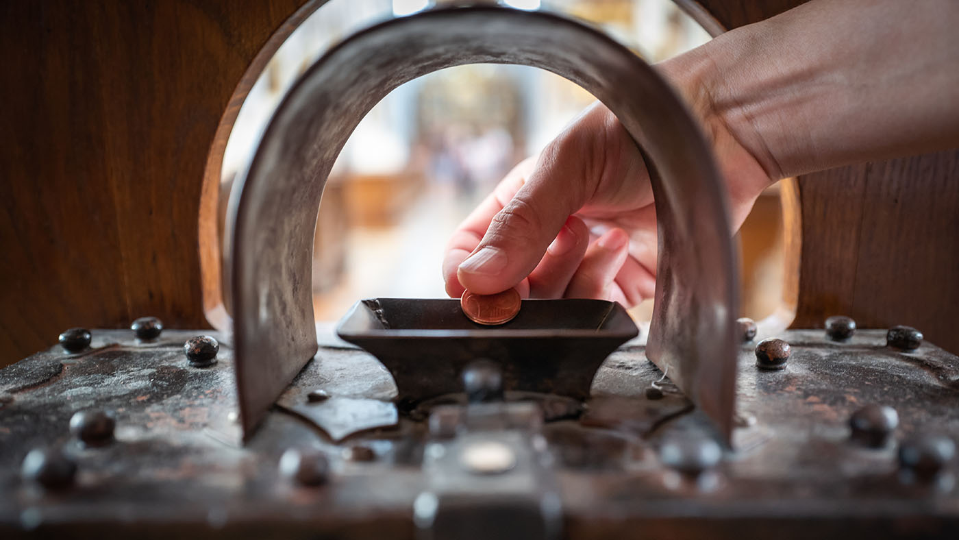 a hand dropping a coin into a donation box