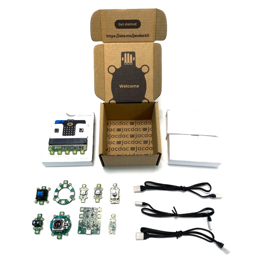 The Jacdac hardware kit. It features a brown cardboard box, containing a BBC micro:bit, some jacdac cables, and some Jacdac hardware modules