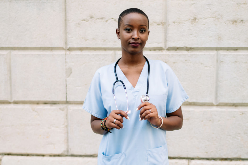 a medical professional in scrubs holding a stethoscope posing for the camera