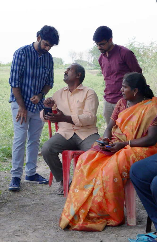 Saiprasad Chirivirala of Digital Green (standing, left) and Arnab Paul Choudhury of Microsoft Research (standing, right) demonstrate FarmerChat during a field visit with farmers.