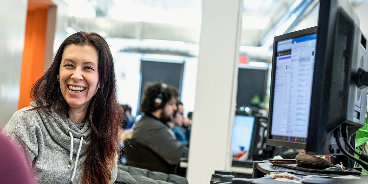 Image of a woman in an IT department smiling at her desk.