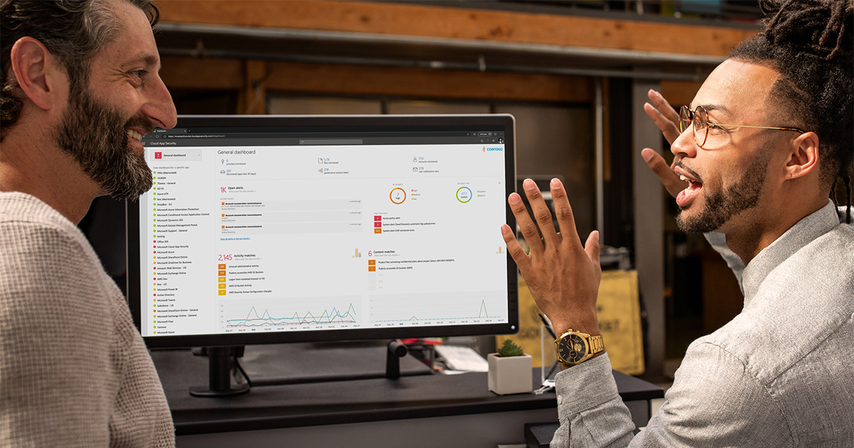 Image of two workers talking next to a computer monitor.