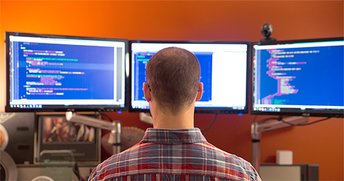 An IT professional working on a multi-screen PC workstation.