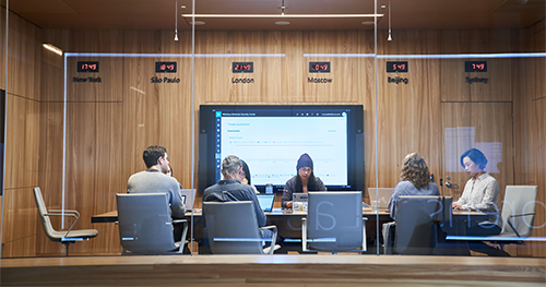 An image of a conference room or board room meeting including people sitting around table in a room with international time clocks.