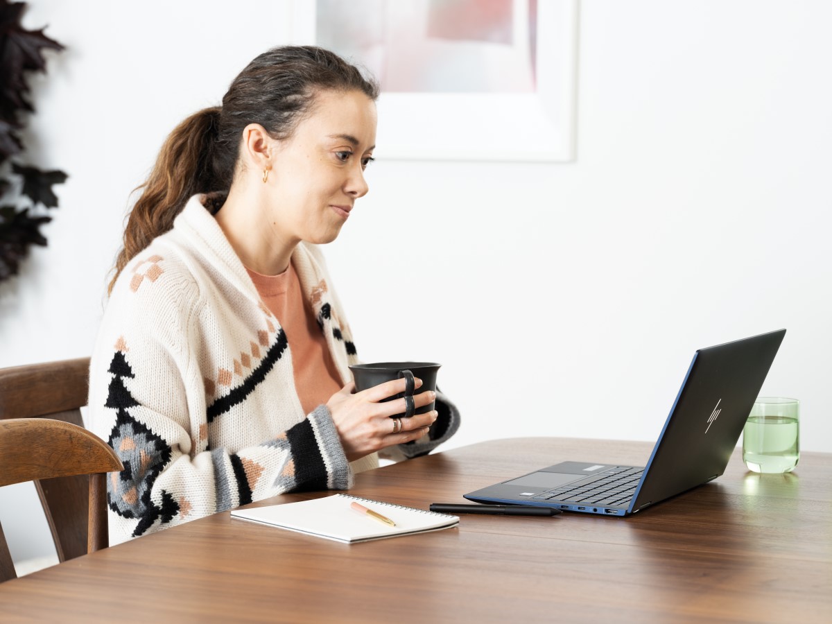 Woman holding a mug with laptop on dining room table with an HP Elite Dragonfly