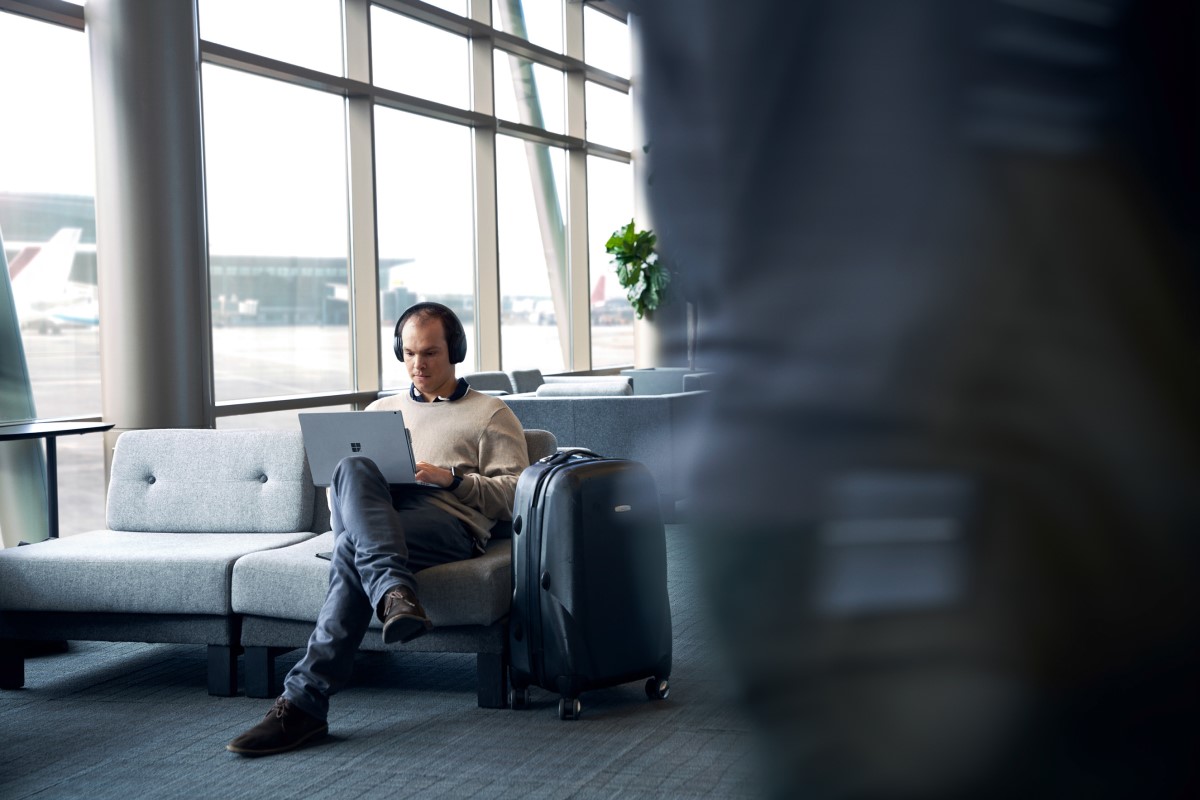 Adult male sitting in airport terminal working on his laptop.