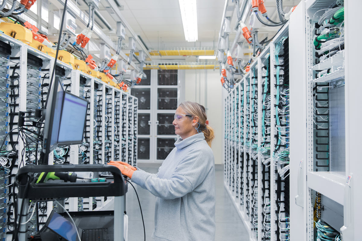 Female datacenter employee performs maintenance in datacenter cold aisle.