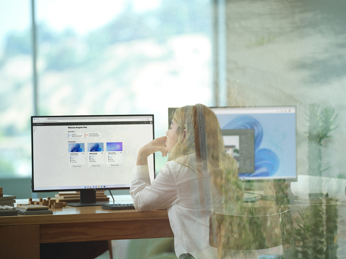 A female architect sitting at an office desk showing Windows 365 and its Welcome screen on dual desktop monitors. Shown on Windows 11.