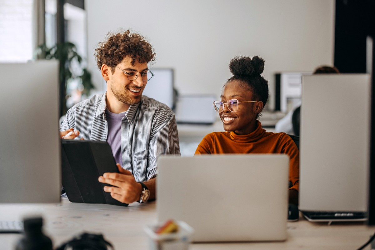 Two people sit behind computers.